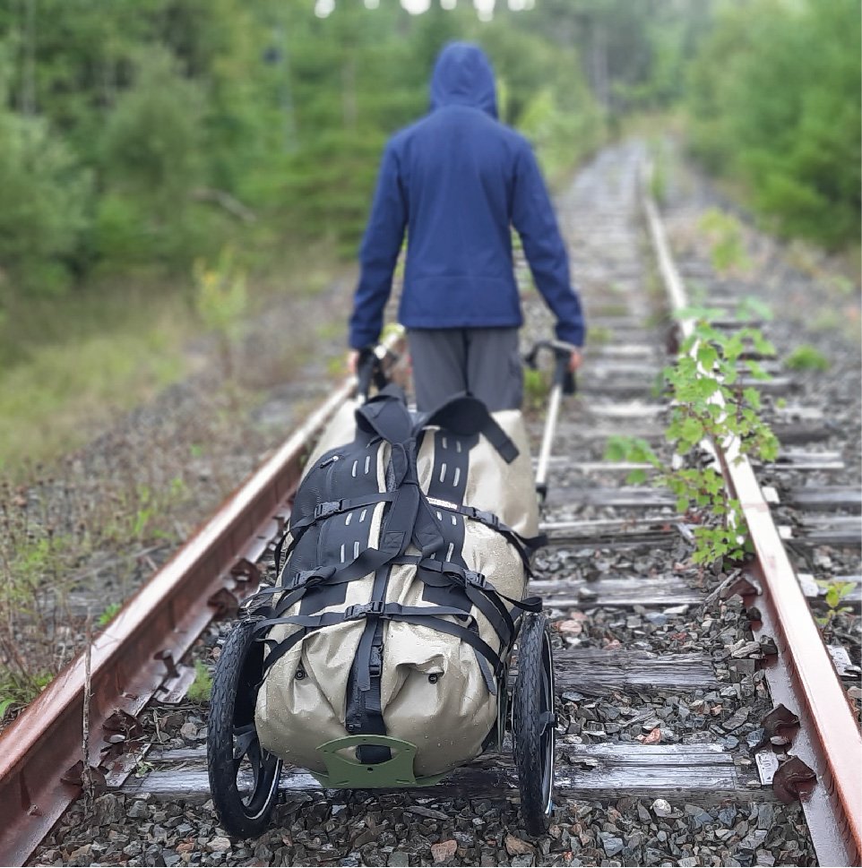Ein Mann läuft auf Bahnschienen und zieht dabei einen Benpacker hinter sich her