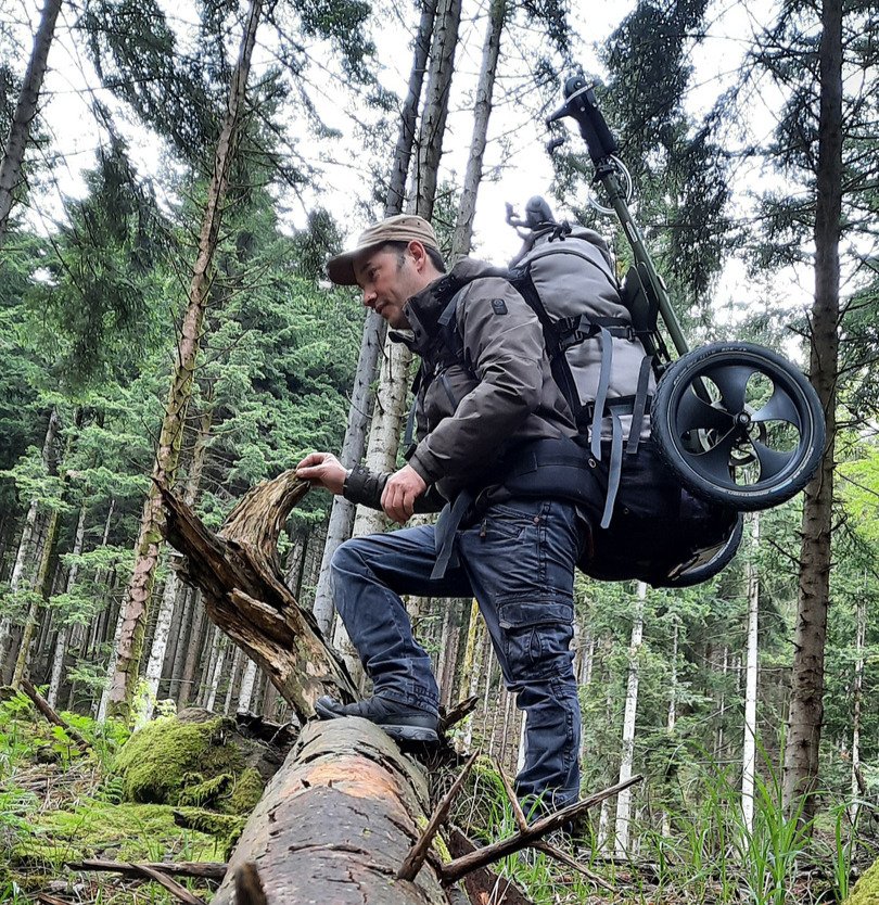 Ben klettert mit dem Benpacker auf dem Rücken über einen Baumstumpf