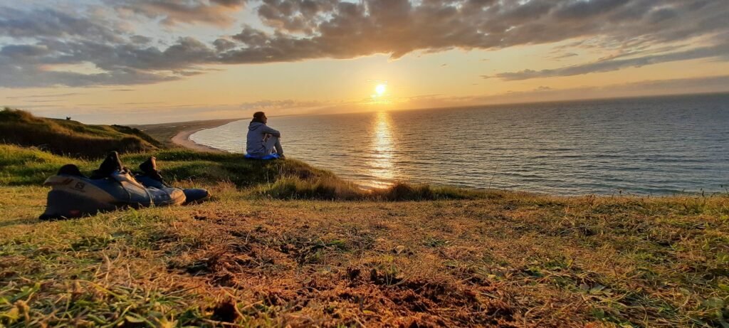 Ein Mann schaut sich am Meer den Sonnenuntergang an